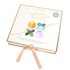 Calendrier de l'Avent Mille et Un Bijoux Omsaé, coffret blanc aux bordures dorées et illustrations colorées de symboles magiques, fermé par un ruban beige. Copier