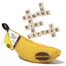 Le jeu Bananagrams illustré par sa célèbre pochette en tissu jaune vif en forme de banane, ornée du logo ovale du jeu. Une étiquette attachée à la fermeture éclair indique qu'il s'agit de la version française. Juste au-dessus, plusieurs tuiles carrées de 